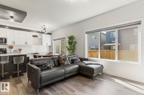 Open-concept living area with wood-finish flooring, a large window, and high-gloss white cabinetry - 19703 29 Avenue Nw, Edmonton, AB 