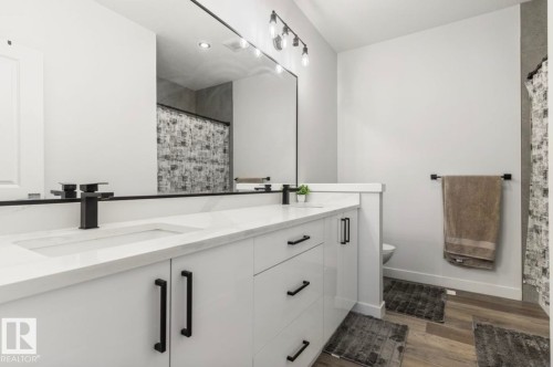 Dual vanity with integrated sinks, white cabinetry, matte black hardware, track lighting, and wood-finish flooring - 19703 29 Avenue Nw, Edmonton, AB 