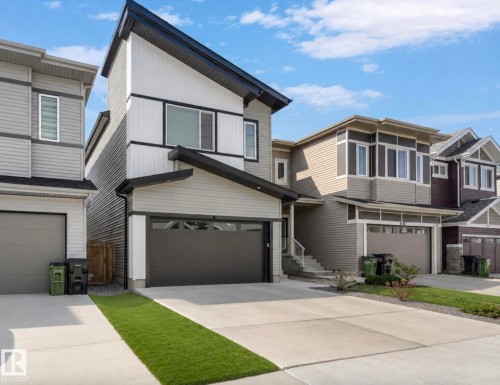 Contemporary exterior featuring multiple siding textures, an attached garage with a dark panel door, a sloped roofline, and a concrete driveway - 19703 29 Avenue Nw, Edmonton, AB 
