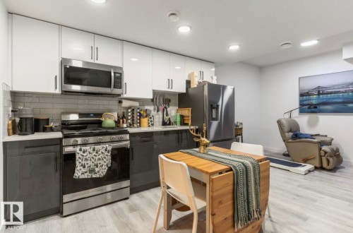Contemporary kitchen featuring two-tone cabinetry, stainless steel appliances, a subway tile backsplash, and light wood-finish flooring - 19703 29 Avenue Nw, Edmonton, AB 