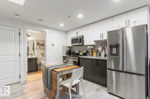 Modern kitchen featuring white upper cabinetry, dark lower cabinetry, stainless steel appliances, and wood-finish flooring - 19703 29 Avenue Nw, Edmonton, AB 