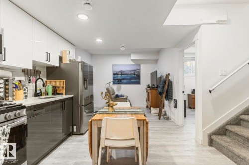 Modern kitchen featuring white upper cabinetry, dark lower cabinetry, stainless steel appliances, and a tile backsplash - 19703 29 Avenue Nw, Edmonton, AB 