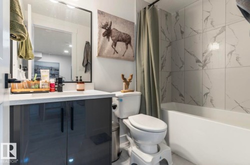 Bathtub with tile surround, white toilet, and vanity with built-in sink and dark cabinetry - 19703 29 Avenue Nw, Edmonton, AB 