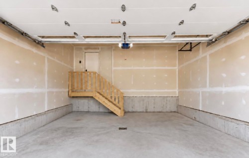 Spacious garage featuring a concrete floor, exposed drywall, a wooden staircase, and an automatic garage door opener - 19703 29 Avenue Nw, Edmonton, AB 