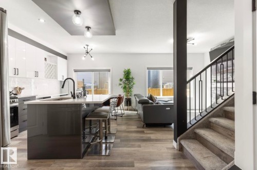 Gourmet kitchen with sleek white cabinetry, large center island with seating, and stainless steel appliances - 19703 29 Avenue Nw, Edmonton, AB 