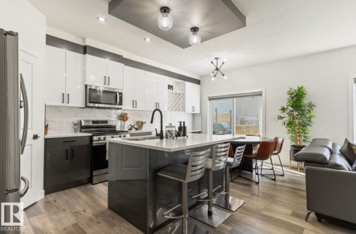 Modern kitchen featuring white and dark gray cabinetry, stainless steel appliances, a white subway tile backsplash, and wood-finish flooring - 19703 29 Avenue Nw, Edmonton, AB 