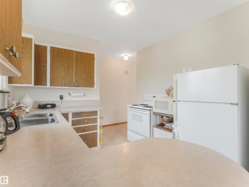 Kitchen featuring wood-finish cabinetry, a double basin sink, and laminate countertops - 12614 69 Street Nw, Edmonton, AB 