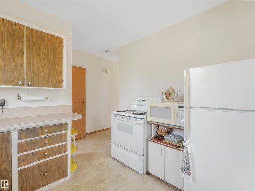 Kitchen featuring wood-finish cabinetry, light-toned countertops, and a white appliance suite - 12614 69 Street Nw, Edmonton, AB 
