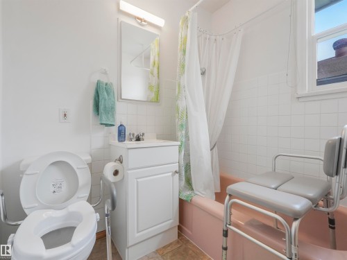 White tile bath surround, window, built-in vanity with sink and faucet, flush-mount lighting, and neutral tone flooring - 12614 69 Street Nw, Edmonton, AB 