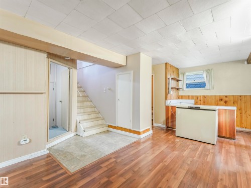 Wood-finish flooring, staircase with carpeted treads, paneled walls, built-in shelving, and a window with blinds - 12614 69 Street Nw, Edmonton, AB 