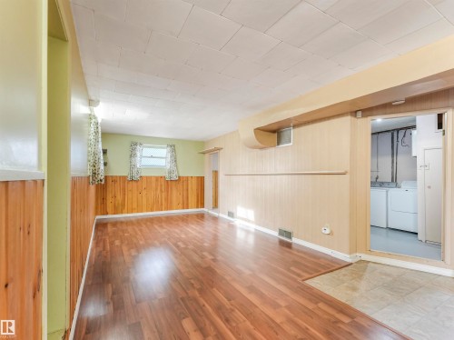 Spacious room featuring wood-finish flooring, two windows, wood paneling, and a drop ceiling - 12614 69 Street Nw, Edmonton, AB 