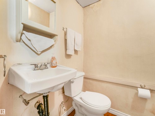 Pedestal sink with chrome faucet, wall-mounted mirror, white toilet, and wood-finish flooring - 12614 69 Street Nw, Edmonton, AB 