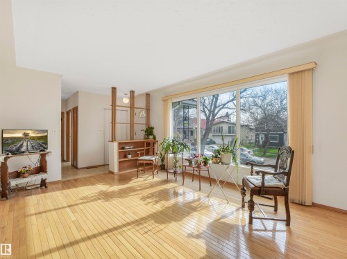 Expansive living area featuring light wood-finish flooring, a full-height picture window, and a built-in room divider with shelving - 12614 69 Street Nw, Edmonton, AB 