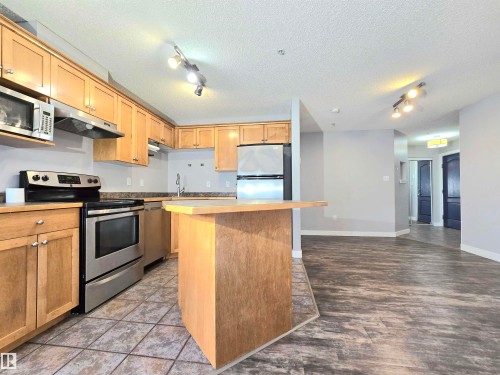 Kitchen featuring stainless steel appliances, light wood cabinetry, a breakfast bar, and tile flooring - #105 155 Edwards Dr Sw, Edmonton, AB - Indoor Photo Showing Kitchen