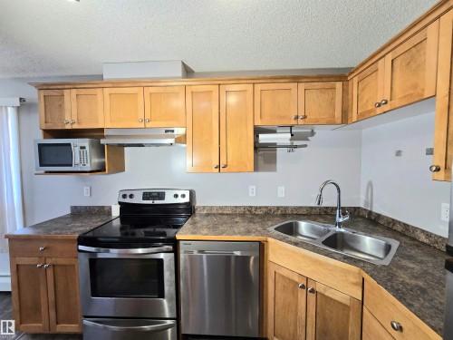 Kitchen featuring light wood cabinetry, stainless steel appliances, and a double-basin sink with a high-arc faucet. - #105 155 Edwards Dr Sw, Edmonton, AB - Indoor Photo Showing Kitchen With Double Sink