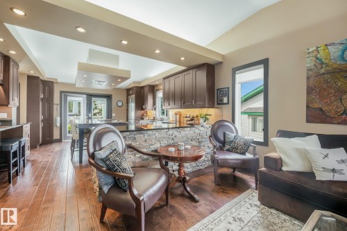 Hardwood-finish flooring throughout, recessed ceiling lighting, kitchen with dark wood-finish cabinetry, stone veneer island base, and glass-paneled double doors - 12827 150 Avenue Nw, Edmonton, AB 