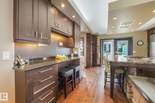 Rich wood-finish flooring, dark wood cabinetry, recessed lighting, stone-clad kitchen island, and glass-paned double doors - 12827 150 Avenue Nw, Edmonton, AB 