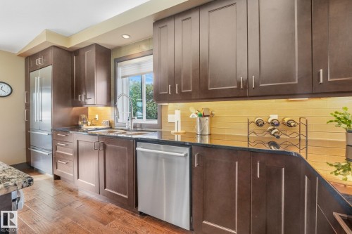 Hardwood-style flooring, dark wood-finish cabinetry, stainless steel appliances, dark countertops, and a tiled backsplash - 12827 150 Avenue Nw, Edmonton, AB 
