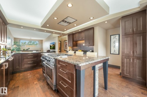 Expansive kitchen featuring wood-finish flooring, dark wood cabinetry, a large kitchen island with a granite countertop, and stainless steel appliances - 12827 150 Avenue Nw, Edmonton, AB 