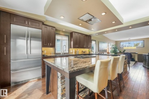 Kitchen featuring a stainless steel refrigerator, dark wood-finish cabinetry, a large center island with a speckled countertop, and wood-finish flooring - 12827 150 Avenue Nw, Edmonton, AB 