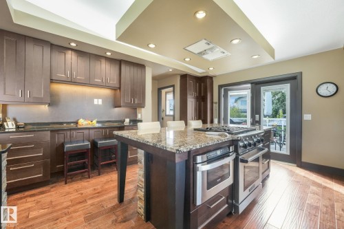 Expansive kitchen featuring dark wood cabinetry, a large kitchen island with a stone countertop, stainless steel appliances, and wood-finish flooring - 12827 150 Avenue Nw, Edmonton, AB 