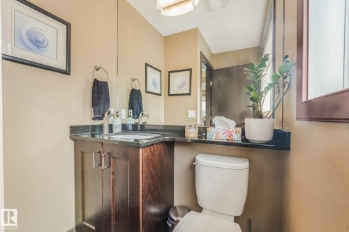 Wood-finish vanity with a drop-in sink, dark countertop, and a wall-mounted mirror - 12827 150 Avenue Nw, Edmonton, AB 