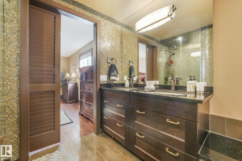 Dual vanity with dark wood-finish cabinetry, integrated sinks, and dark stone countertops - 12827 150 Avenue Nw, Edmonton, AB 