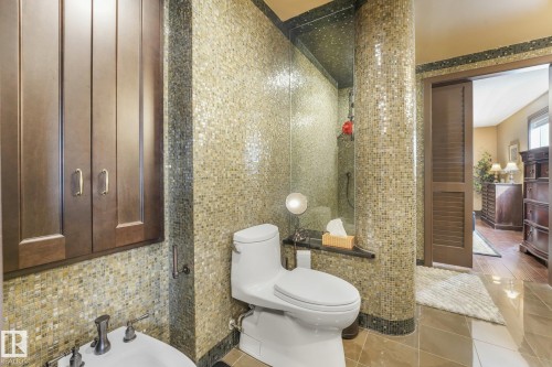 Mosaic tile walls, white ceramic toilet, bidet fixture, dark wood cabinetry with gold-toned hardware, and a dark wood louvered door - 12827 150 Avenue Nw, Edmonton, AB 