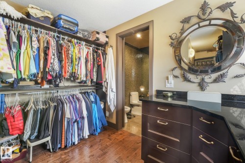 Wood-finish flooring with built-in dark wood cabinetry, a dark countertop, and a decorative wall mirror - 12827 150 Avenue Nw, Edmonton, AB 