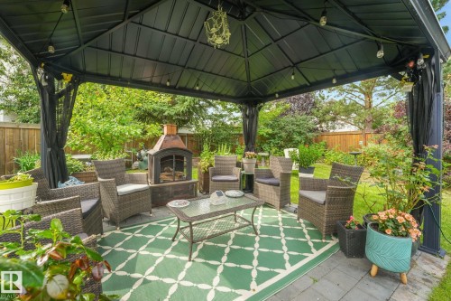 Paved patio area featuring a black metal gazebo, integrated string lighting, and a built-in outdoor fireplace - 12827 150 Avenue Nw, Edmonton, AB 