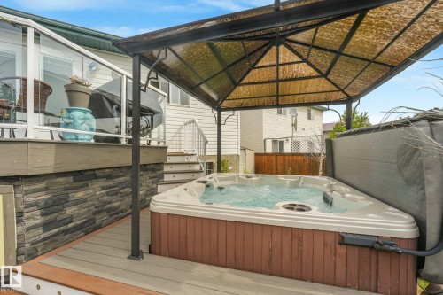 Hot tub with a protective canopy, set on a multi-level deck with a glass railing - 12827 150 Avenue Nw, Edmonton, AB 