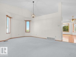 Vaulted ceiling with an orb pendant light fixture, large windows with wood trim, and light-colored carpeting - 