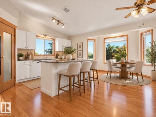AI GENERATED PHOTO -Open-concept area featuring wood-finish flooring, white cabinetry, a kitchen island with seating, a dining area with a bay window, and a vaulted ceiling - 535 Pardee Bay Nw, Edmonton, AB 