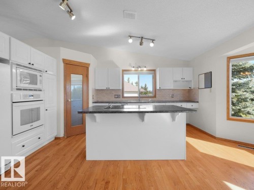 White cabinetry, a center island with a dark countertop, integrated double oven and microwave, wood-finish flooring, and recessed lighting - 535 Pardee Bay Nw, Edmonton, AB 