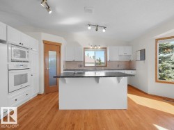 White cabinetry, a center island with a dark countertop, integrated double oven and microwave, wood-finish flooring, and recessed lighting - 