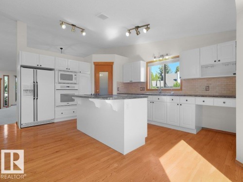 Bright kitchen featuring white cabinetry, a central island with a contrasting countertop, wood-finish flooring, and built-in appliances - 535 Pardee Bay Nw, Edmonton, AB 