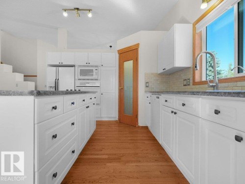 White cabinetry, integrated appliances, light gray countertops, wood-finish flooring, and a subway tile backsplash - 535 Pardee Bay Nw, Edmonton, AB 