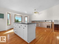 Spacious room featuring wood-finish flooring, a white kitchen island with a dark countertop, large windows, and a high ceiling - 