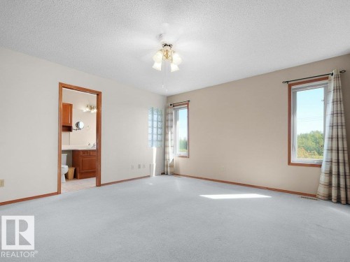 Carpeted flooring, ceiling fan with integrated lighting, multiple windows, and an adjacent bathroom with a vanity and sink - 535 Pardee Bay Nw, Edmonton, AB 
