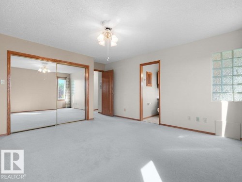 Light-colored carpeted flooring, mirrored closet doors with wood trim, wood-trimmed doorways, and a glass block window - 535 Pardee Bay Nw, Edmonton, AB 