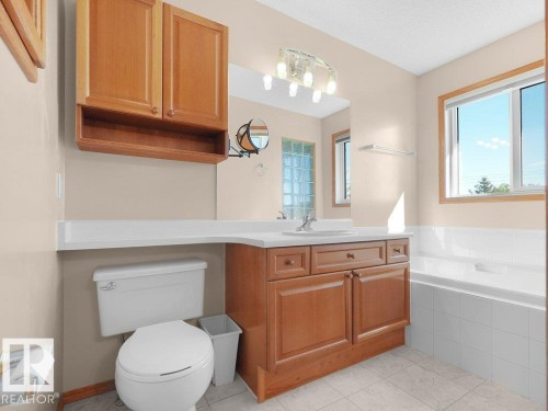 Bathroom with a window, built-in bathtub, wood-finish vanity with countertop, wall-mounted mirror, and overhead lighting - 535 Pardee Bay Nw, Edmonton, AB 