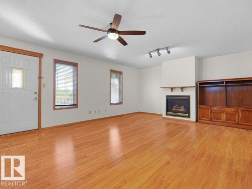 Wood-finish flooring, ceiling fan with integrated lighting, two windows with blinds, built-in entertainment center, and a fireplace with a mantel - 535 Pardee Bay Nw, Edmonton, AB 