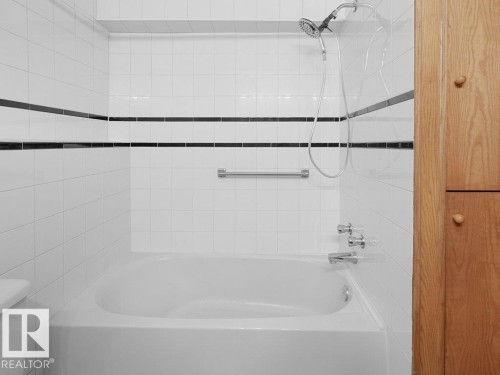 Bathtub with chrome fixtures, white subway tile surround, decorative black accent tiles, and a natural wood-finish storage cabinet - 535 Pardee Bay Nw, Edmonton, AB 