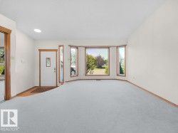 Recessed ceiling lighting, white interior walls, bay window with wood-finish trim, wood-finish flooring, and a white entrance door with a decorative glass insert - 