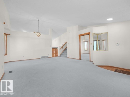 Expansive carpeted area with vaulted ceilings, a central chandelier, wood-trimmed windows, and a staircase - 535 Pardee Bay Nw, Edmonton, AB 