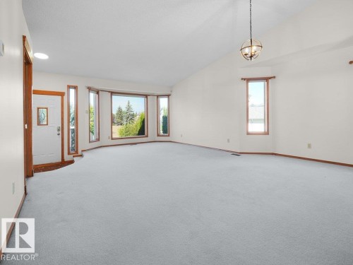 Vaulted ceiling with an orb chandelier, bay window, white entry door with a decorative glass insert, and light-colored carpeting - 535 Pardee Bay Nw, Edmonton, AB 