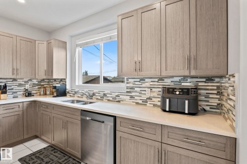 Contemporary cabinetry with light wood-finish doors, durable countertops, mosaic tile backsplash, and a stainless steel dishwasher - 10338 162St Nw, Edmonton, AB 