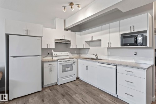 Kitchen featuring white cabinetry, wood-finish flooring, white appliances, and a built-in microwave - 10338 162St Nw, Edmonton, AB 