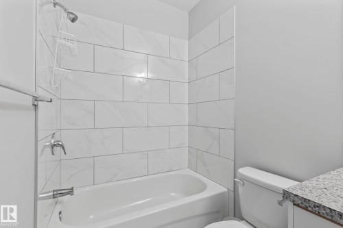 Bathtub with subway tile surround and chrome fixtures, adjacent to a toilet and vanity with a granite-style countertop - 10338 162St Nw, Edmonton, AB 