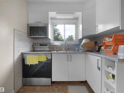 Kitchen featuring a stainless steel range, stainless steel microwave, white cabinetry, light-colored countertops, and a white subway tile backsplash - 12002 48 Street Nw, Edmonton, AB 